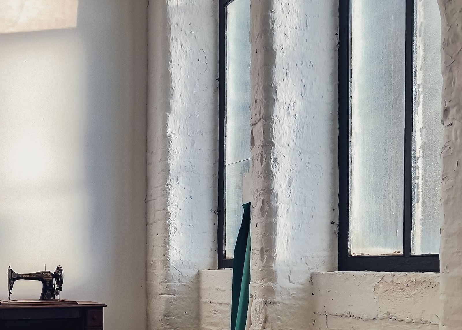 Tall mill windows over whitewashed brick, with an old sewing machine