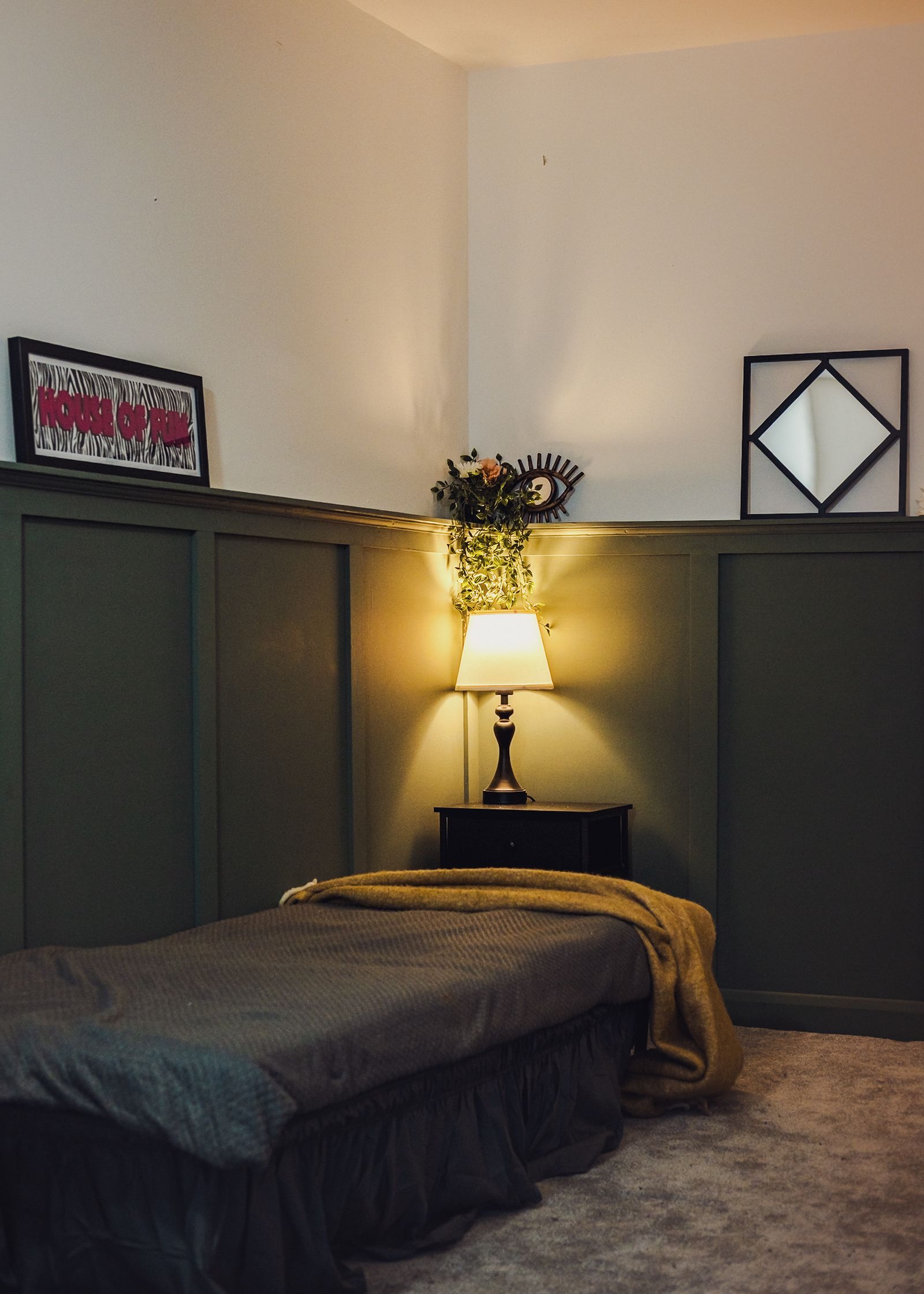 A corner of the bedroom set with a lamp, flowers and dark green panelling